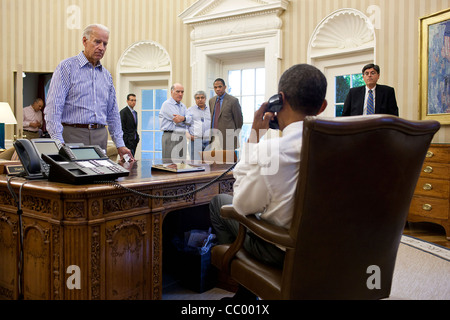 Vice President Joe Biden and other staff watch and listen as the President Barack Obama talks on the phone in the Oval Office with Senate Majority Leader Harry Reid during the debt limit and deficit discussions July 31, 2011 in Washington, DC. Stock Photo