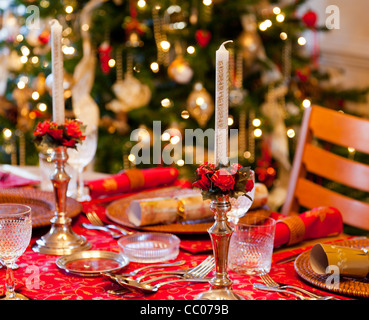 Christmas table setting for Christmas dinner with candles, crackers and tree in background Stock Photo