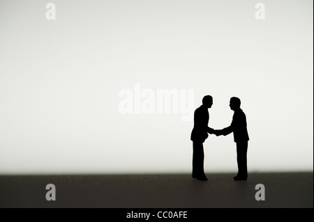 silhouetted small figures conceptual image for two business men meeting agreeing a deal shaking hands