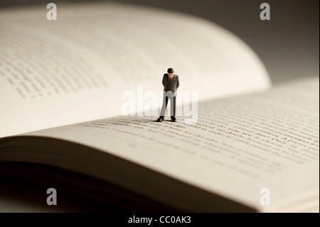 a small figure of a man walking on an open book - conceptual image for literacy and reading Stock Photo