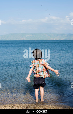 Boy playing in water - throwing stones in the Sea of Galilee, Kineret, Northern Israel Stock Photo