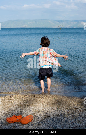 Boy playing in water, throwing stones, Sea of Galiliee, Kineret, Israel Stock Photo