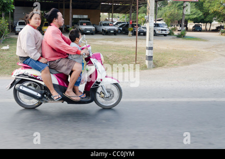 A man & woman and small boy in front traveling on a motorbike in northern Thailand. The woman is looking at the camera. Stock Photo