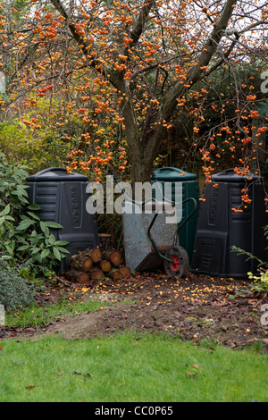 Garden compost bins under a crab apple tree with logs and a wheel barrow. A typical English country garden scene. Stock Photo