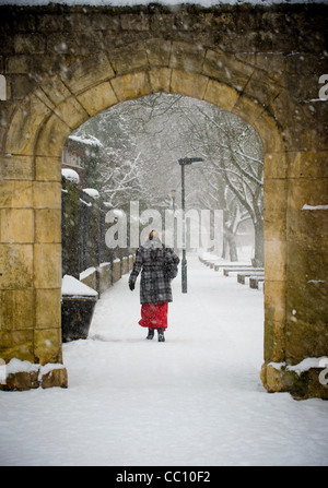 Rear view of a mature woman walking through the medieval archway along the bank of the river Ouse, in a snow shower, York. Stock Photo