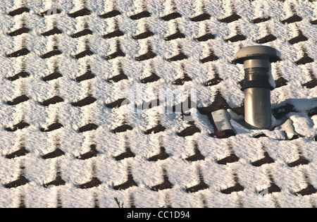 Snow covered tiled roof with central heating vent chimney Stock Photo
