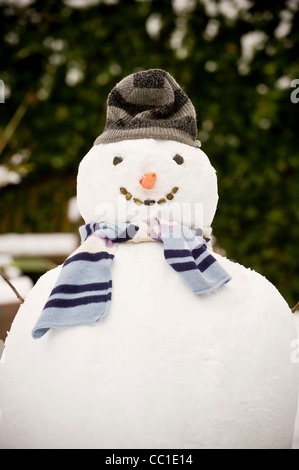Snowman wearing a grey striped hat and a blue striped scarf in a UK garden. Stock Photo