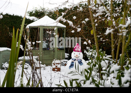 Snow covered greenhouse with snowman in the foreground of a UK garden in winter. Stock Photo