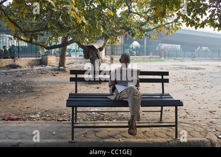 An old man reads a newspaper on a park bench in the early morning in New Delhi, India. Stock Photo