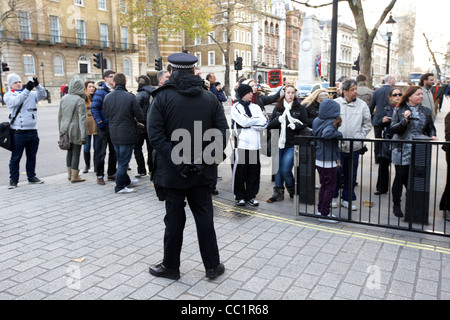 metropolitan police officer stands guard watching tourists outside the gates of downing street at whitehall London England UK Stock Photo