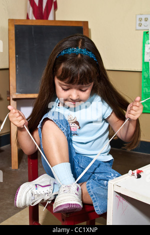 4-5 year old girl learning to tie her shoes laces shoelaces  in interracial classroom. POV  MR  © Myrleen Pearson Stock Photo