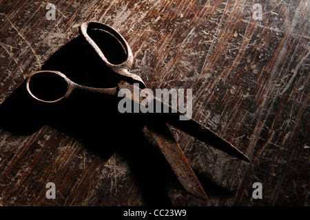 Pair of rusty scissors on old, scratched, wooden tabletop Stock Photo