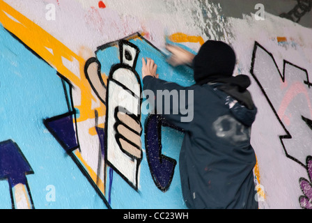 Tagging - Hooded young man spray painting graffiti. Note: Parts of man in blurred motion. Note: Parts of man in blurred motion. Stock Photo