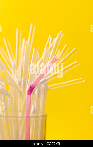A pink straw amongst a group of clear straws
