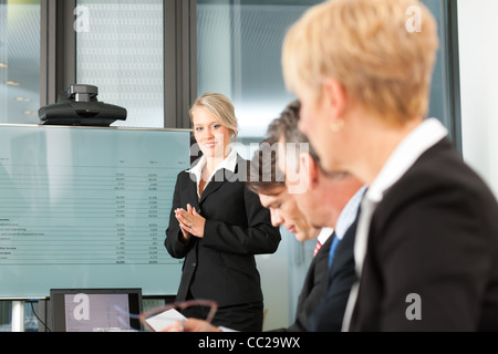 Business - presentation within a team; a female, colleague is standing on the screen Stock Photo