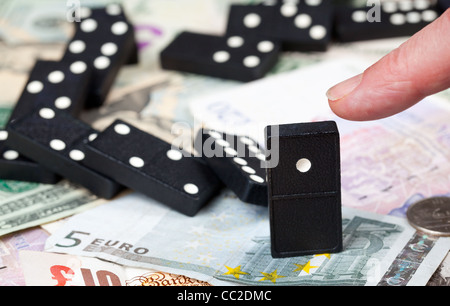Finger pushing last domino standing on pound, euro and dollar bank notes illustrating banking crisis Stock Photo