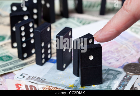 Finger pushing standing dominoes on pound, euro and dollar bank notes illustrating banking crisis Stock Photo