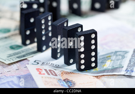 Standing dominoes on pound, euro and dollar bank notes illustrating banking crisis Stock Photo