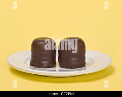 two small chocolate-covered cream cakes on a plate Stock Photo