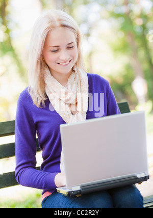 USA, New York, New York City, Manhattan, Central Park, Young woman sitting on bench and using laptop Stock Photo
