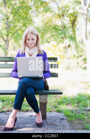 USA, New York, New York City, Manhattan, Central Park, Young woman sitting on bench and using laptop Stock Photo