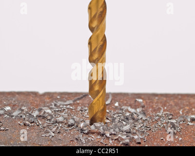 a golden drill is in a piece of metal, cuttings alongside Stock Photo
