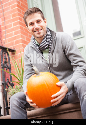 USA, New Jersey, Jersey City, Man sitting on steps with pumpkin Stock Photo