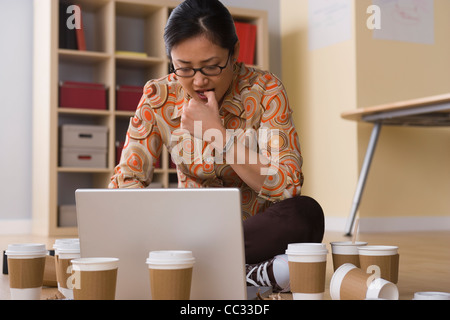 USA, California, Los Angeles, Woman working on laptop surrounded by empty coffee cups Stock Photo