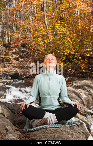 USA, New Jersey, Woman meditating by stream in forest Stock Photo