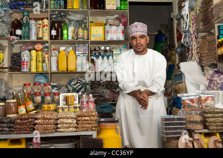 An Arab merchant sitting among his merchandise at a market stall on the bazar of Nizwa, Sultanate of Oman Stock Photo