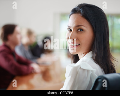 Attractive young Asian business woman smiling and looking over shoulders at business meeting with co-workers. Stock Photo