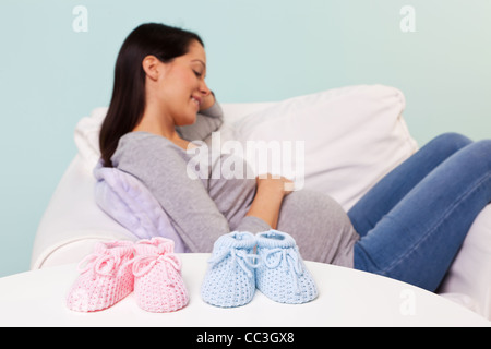 Photo of a pregnant woman at home sitting in an armchair with the focus on a pair of boy and girl knitted baby booties Stock Photo