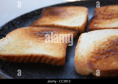 Close up detail shot of four slices of bread being toasted on a pan. Toast is uneven with visible portions of burnt patches. Stock Photo