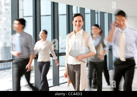 Businesswoman in hallway with blurred business people walking around her Stock Photo