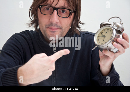 Man showing at the clock with his index finger, indicating that it is too late.