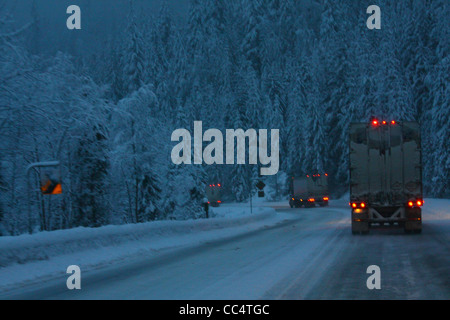 40,524.02077 3 three 18 wheelers trucks curve night snow storm slick ice covered 2-lane rural road chains snowing lights on dangerous travel Stock Photo