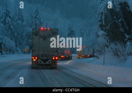 40,524.02083 3 three 18 wheelers trucks curve night snowstorm slick ice covered 2-lane rural road chains snowing lights on dangerous travel Stock Photo