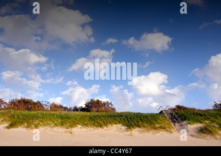 Coastal dunes and stairs leading up covered with sea sand. Blue sky with clouds. Stock Photo