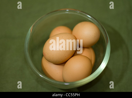 A clear glass bowl of half a dozen eggs on a rustic green linen background Stock Photo