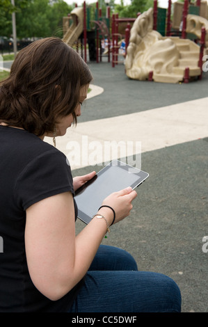 Caucasian woman sitting on a park bench reading her iPad Stock Photo
