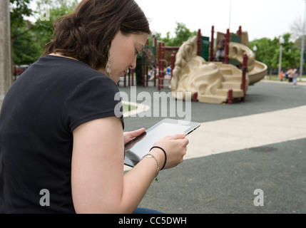 Caucasian woman sitting on a park bench reading her iPad Stock Photo