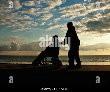 Disabled person in a wheelchair at sunset looking at sea Stock Photo ...