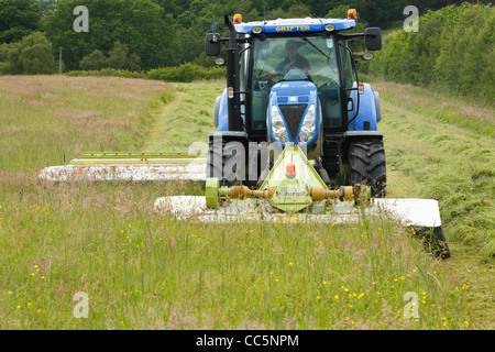 Contractor with New Holland T6080 tractor and front and rear mounted Claas mowers cutting grass for silage. On an Organic farm. Stock Photo