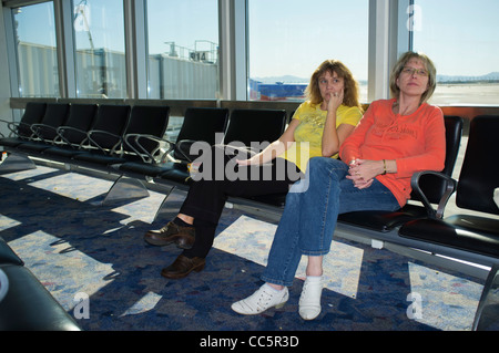 Two women are waiting for boarding time at an airport terminal gate Stock Photo