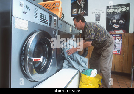 Man putting laundry in washing machine at launderette, Brixton, London, UK. Stock Photo