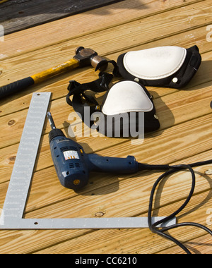 The carpenter's tool laying near where he is working. His hammer, drill, square, and knee pads lay near his work. Stock Photo