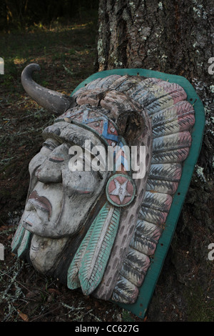 A carved wooden Indian head leaning against a tree. Stock Photo