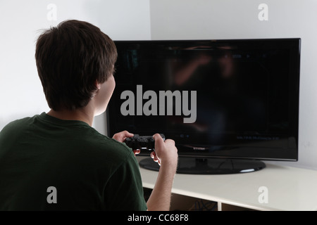 Young male sitting in front of large tv with a game controller in his hand, blank screen ready for your own graphic to be insert Stock Photo