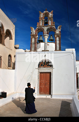 A Greek Orthodox priest tolling the bells of a church in picturesque Pyrgos village, Santorini island, Cyclades, Greece Stock Photo