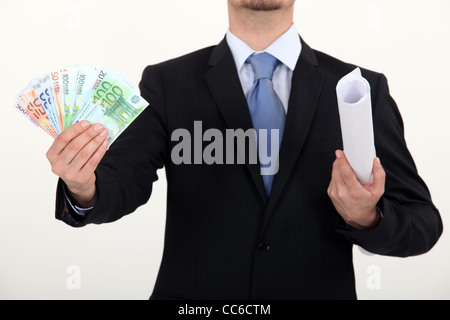 Businessman holding plans and a pile of cash Stock Photo